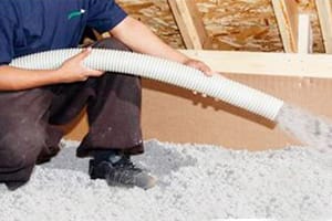 Instalador aplicando celulosa con manguera en un entretecho
